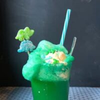 Prehistoric slime soda, dino-fied with green food colouring, a dinosaur gummy swizzle stick, and dinosaur sprinkles